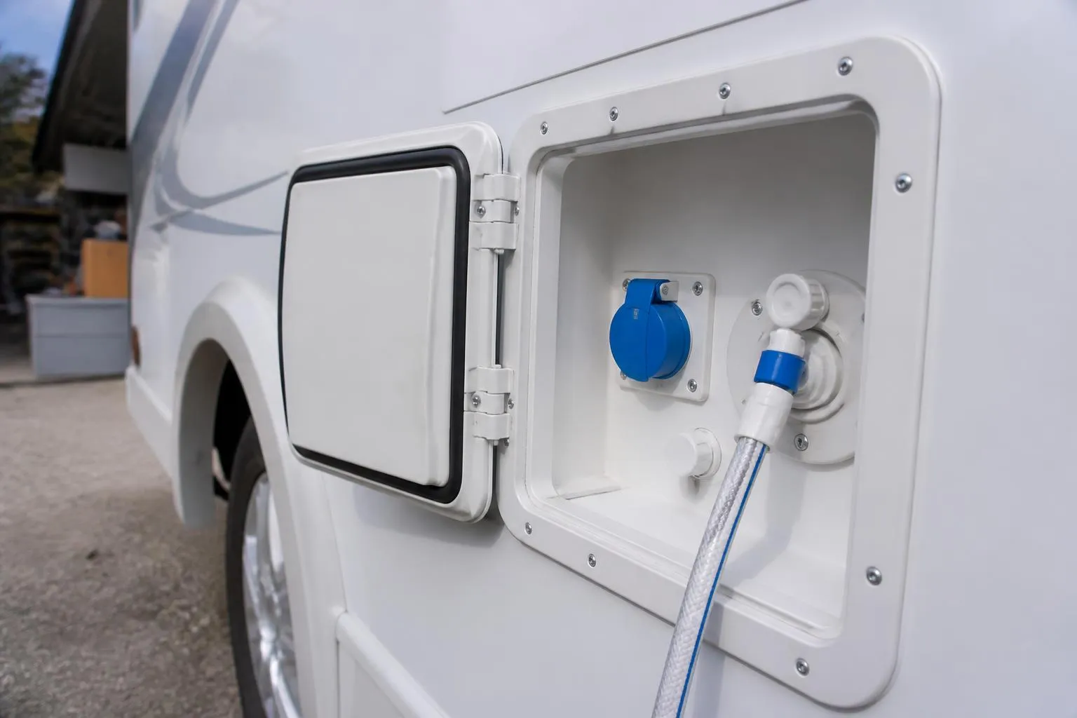 Une trappe de service ouverte sur le flanc d’un camping-car, avec sa prise électrique et son raccord d’eau