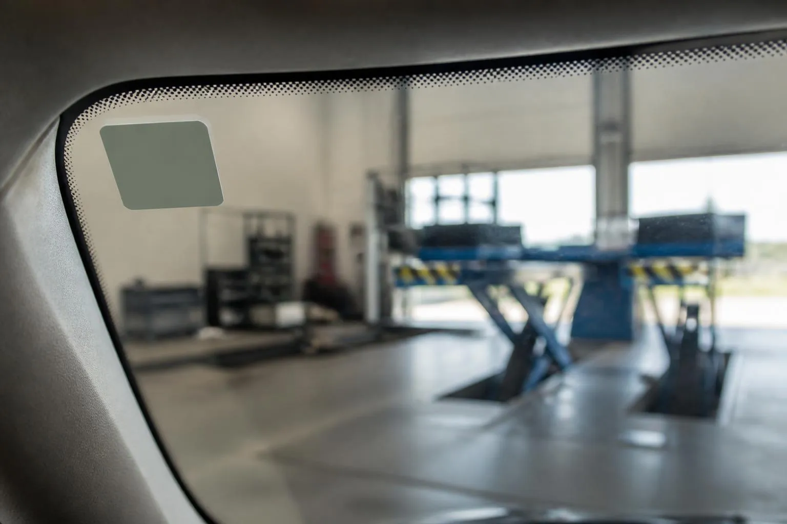Un pare-brise portant sa vignette de contrôle technique, vu depuis l'intérieur d'un atelier