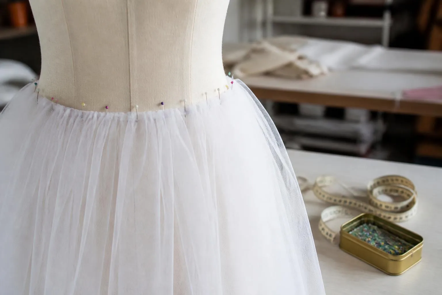 Une jupe de tulle blanc épinglée sur un buste de couture dans un atelier